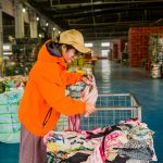 KingAAA quality inspector in orange uniform checking Grade A and Grade B used clothing standards at Guangzhou warehouse.